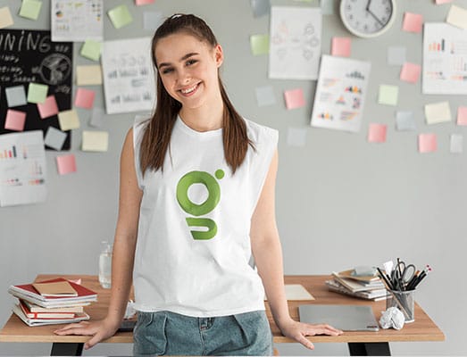 Uśmiechnięta młoda dziewczyna oparta o biurko w białej bluzce z nadrukiem logo Gadżetów reklamowych